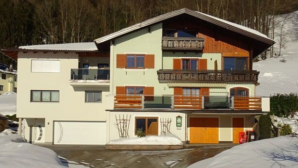 A multi-story building with balconies, a garage, and a snow-covered landscape.