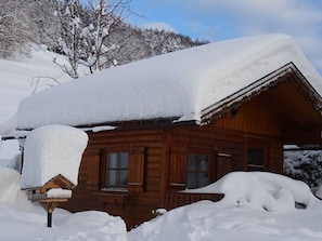 A wooden cabin with a snow-covered roof, surrounded by snow. - Guesthouse Ellmauer Annemarie - Apartment Schafbergblick (Tiefgraben)