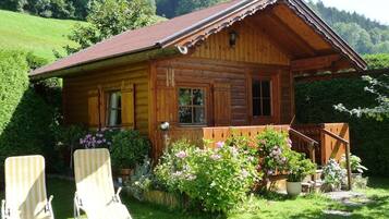 Une cabane en bois avec une véranda, deux fauteuils et un jardin fleuri.
