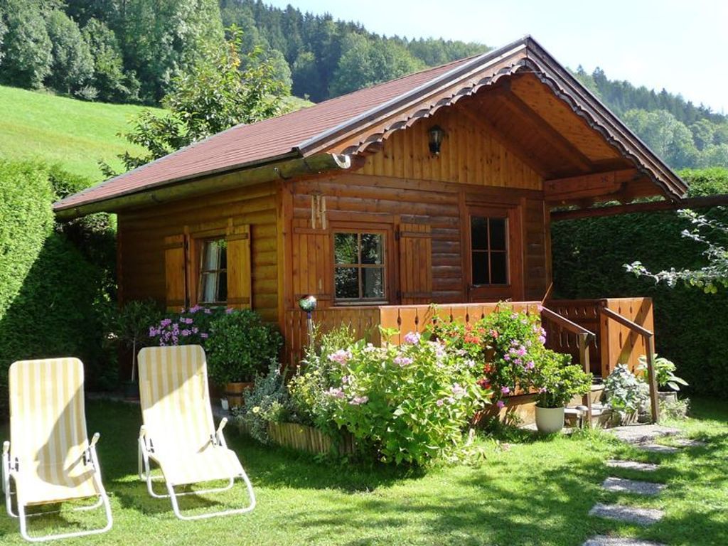 Une cabane en bois avec une véranda, deux fauteuils et un jardin fleuri.