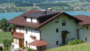 A two-story house with a sloped roof, a balcony, and a view of a lake and mountains.