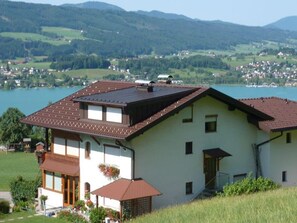 A two-story house with a sloped roof, a balcony, and a view of a lake and mountains.