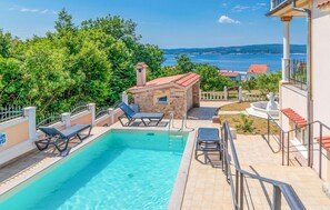 A swimming pool with lounge chairs, a stone building, and a view of the sea.