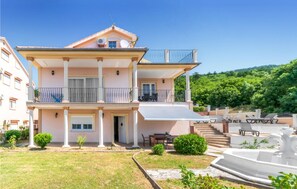 A two-story building with a balcony, a covered patio, and a garden area with a fountain. - Gorgeous home in Dramalj (Dramalj)