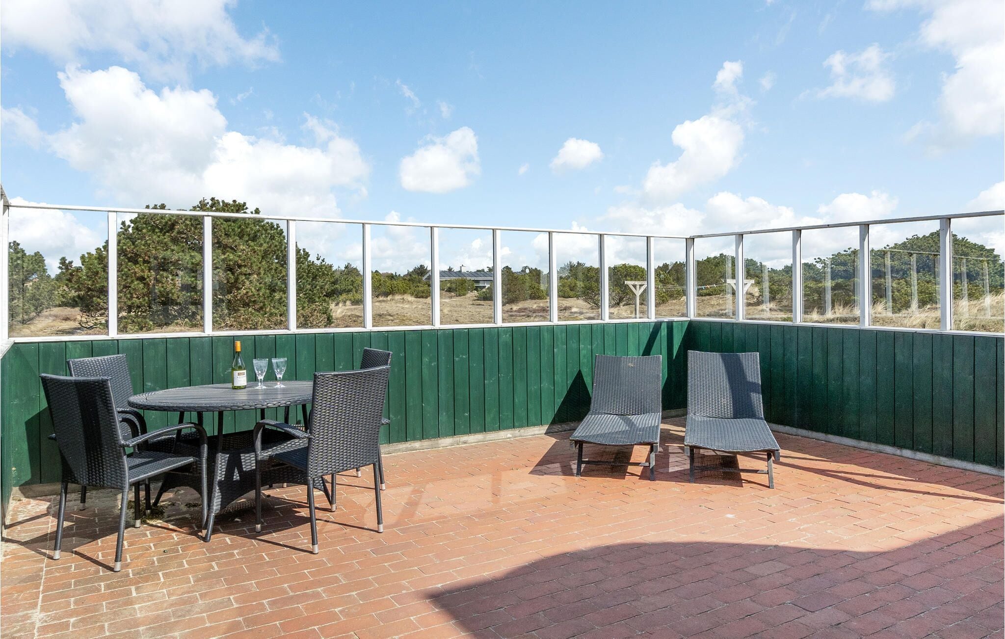Une terrasse extérieure avec un sol en briques, un mur en bois peint en vert et une vue sur la campagne.