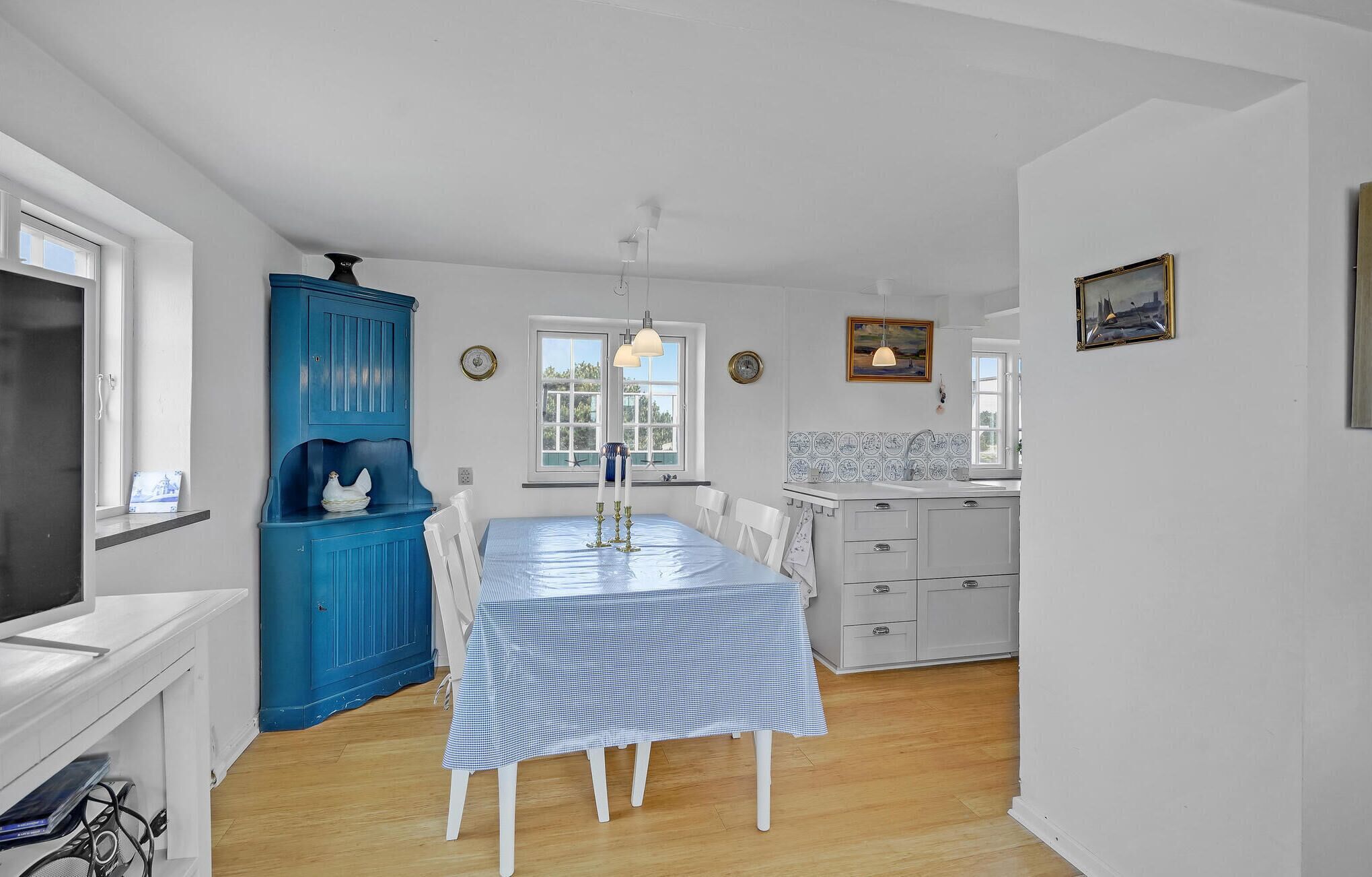 A bright kitchen with a blue cabinet, a dining table with a checkered tablecloth, and a white refrigerator.