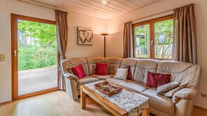 A cozy living room with a leather sofa, a wooden coffee table, and a view of greenery through large windows.