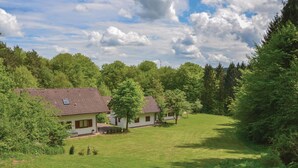 A rural setting with two single-story houses surrounded by lush greenery and a clear sky.