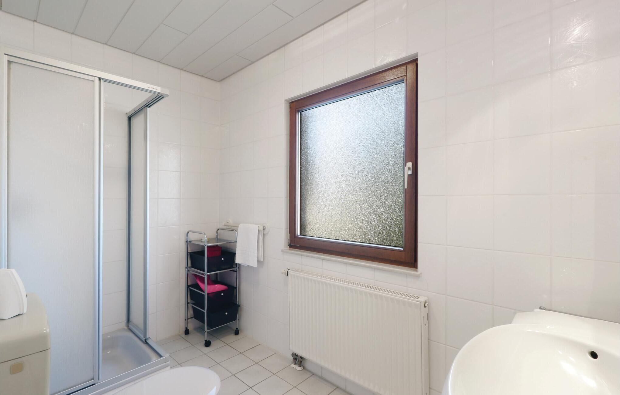 Een badkamer met douche, toilet en een raam.