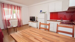 Cocina compacta con armarios blancos, una mesa de comedor de madera y una pared de acento roja.