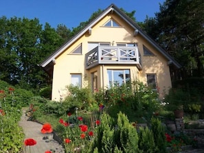 Ein zweistöckiges Haus mit Balkon, umgeben von einem Garten mit roten Blumen.