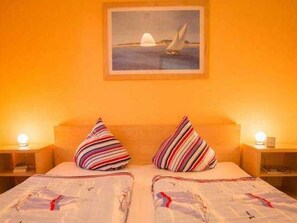 Ein Doppelbett mit gestreiften Kissen, ein gerahmtes Bild eines Segelboots an der Wand und Nachttischlampen.