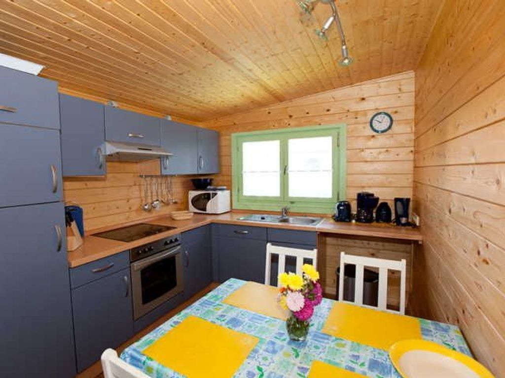 A compact kitchen with wooden walls, a sink, a stove, and a dining table with a yellow tablecloth.