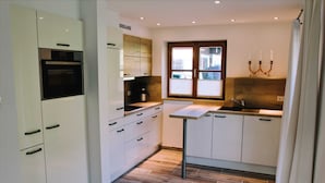 Eine moderne Küche mit weißen Schränken, einem eingebauten Backofen, einer Kaffeemaschine und einem Fenster mit Jalousien.