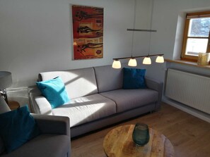 Una sala de estar moderna con un sofá gris, cojines azules, una mesa de centro de madera y un cuadro abstracto colorido en la pared.