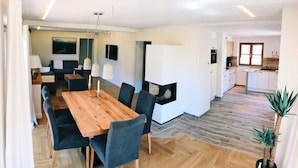 Ein modernes Wohnzimmer mit einem Holzesstisch, dunklen Stühlen, einem Sofa und einem Fernseher.