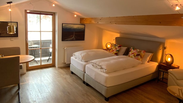 Ein gemütliches Schlafzimmer mit Doppelbett, einem kleinen Tisch und einem Sessel. Ein Fenster bietet Blick ins Freie.