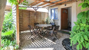 Un patio couvert avec une table et des chaises en bois, un barbecue et une porte donnant sur une pièce.