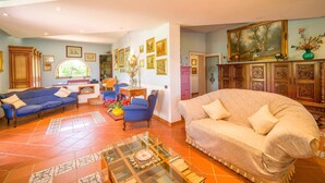 A spacious living room with a large sofa, a smaller sofa, and a coffee table. There are several framed pictures on the walls and a large painting above the fireplace.