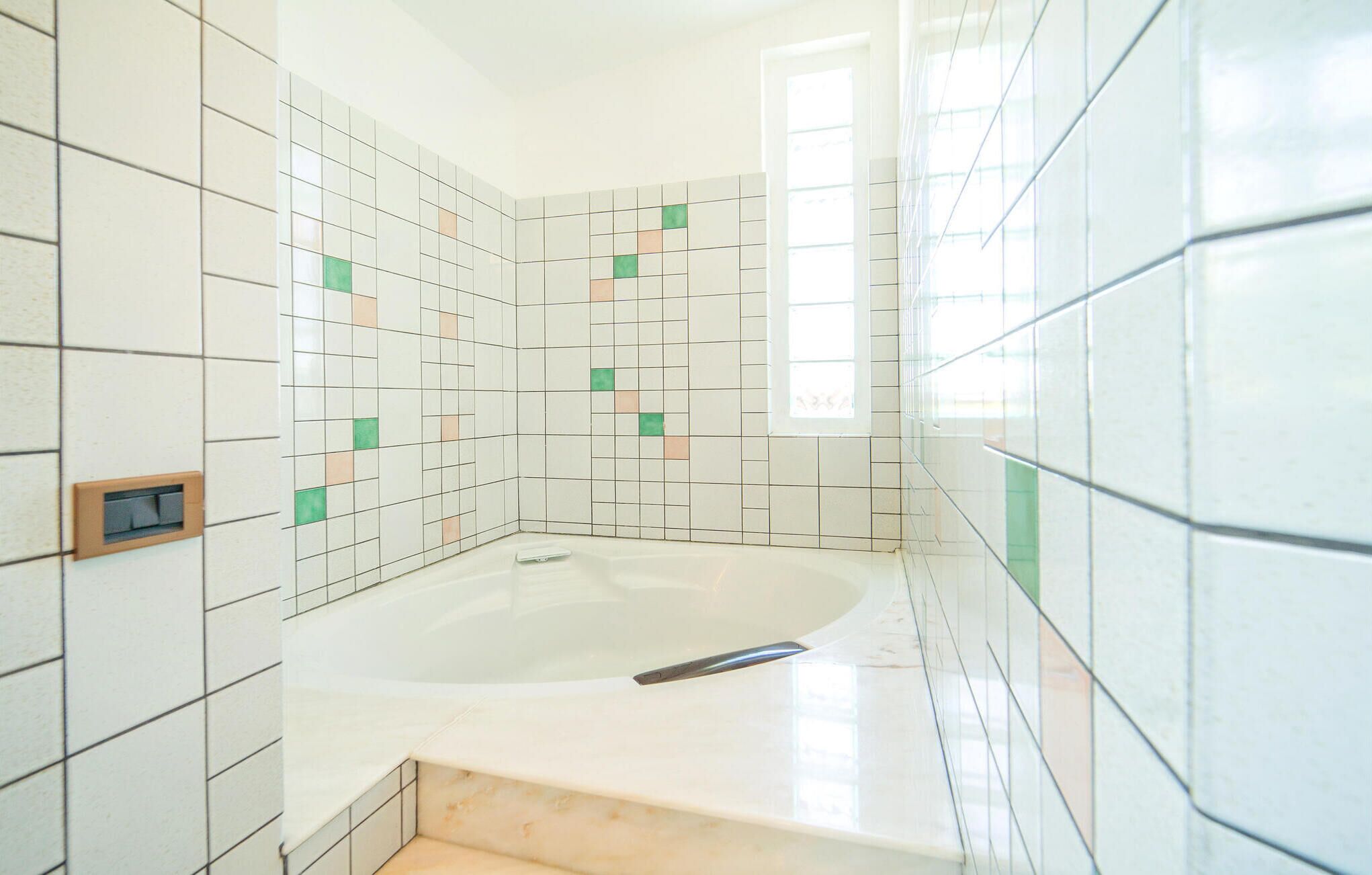 A bathroom with a bathtub, tiled walls, and a window.