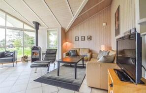 Ein gemütliches Wohnzimmer mit Kamin, bequemen Sitzmöglichkeiten, einem Fernseher und einem großen Fenster mit Blick ins Freie.