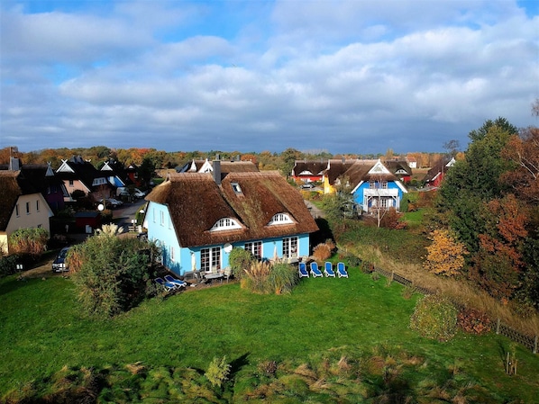 Un pueblo rural con casas tradicionales, un espacio cubierto de césped con sillones de descanso y un cielo despejado.