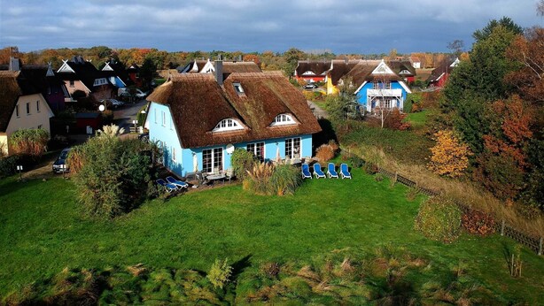 A rural village with traditional houses, a grassy area with lounge chairs, and a clear sky.