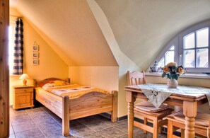 A bedroom with a bed, a wooden nightstand, a table with a vase, and a window.
