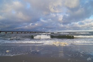 A beach with waves, a pier, and cloudy skies.