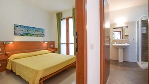 A hotel room with a bed, a painting on the wall, a bathroom with a sink and mirror, and a door leading to another room. - Cozy home in Porto Venere SP with WiFi (Porto Venere SP)