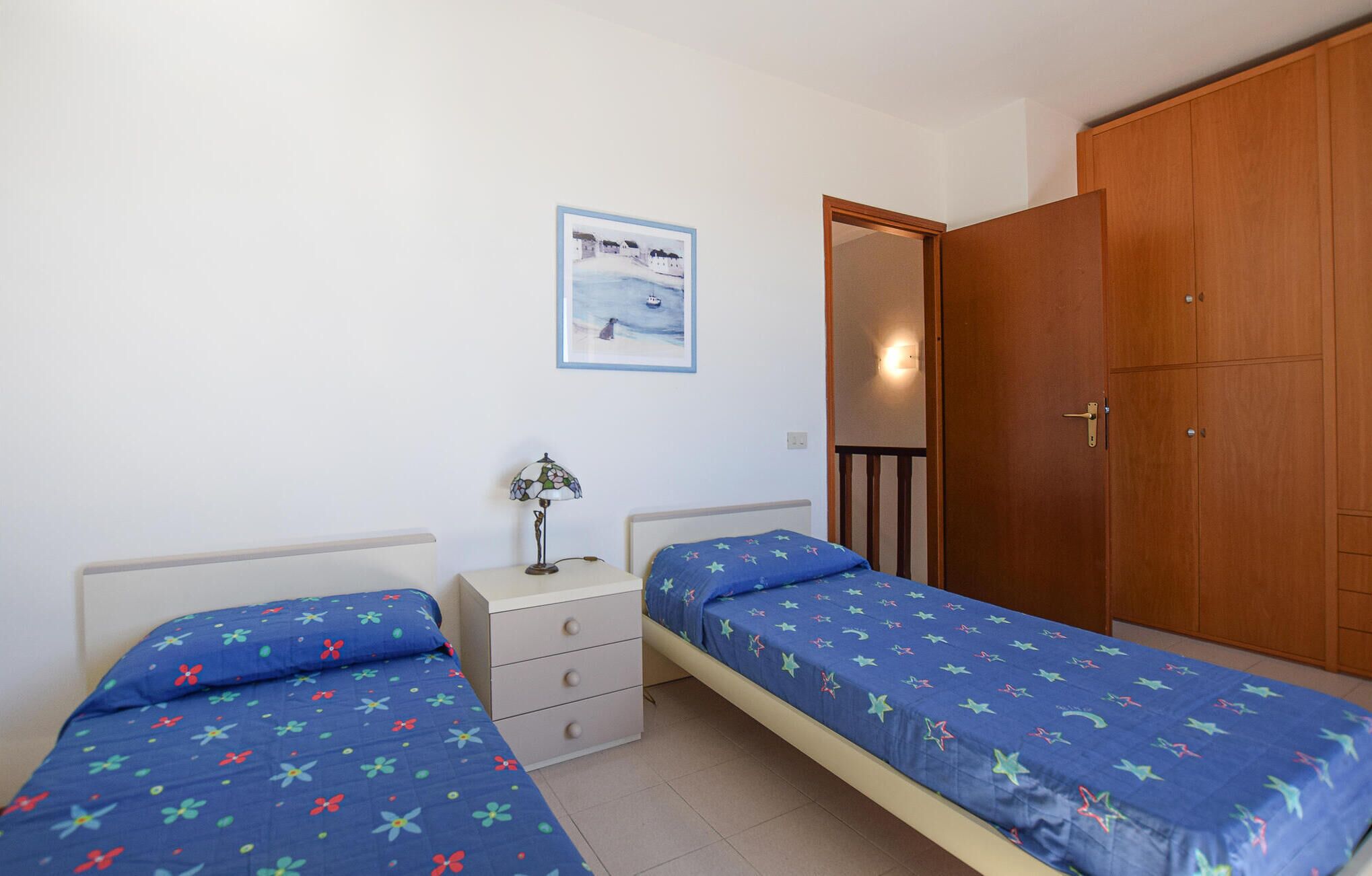 Un dormitorio con dos camas individuales, una mesita de noche, un aparador, un armario de madera y un cuadro en la pared.