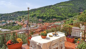 A terrace with a table set for dining, surrounded by potted plants and a scenic view of a hillside town. - Cozy home in Porto Venere SP with WiFi (Porto Venere SP)