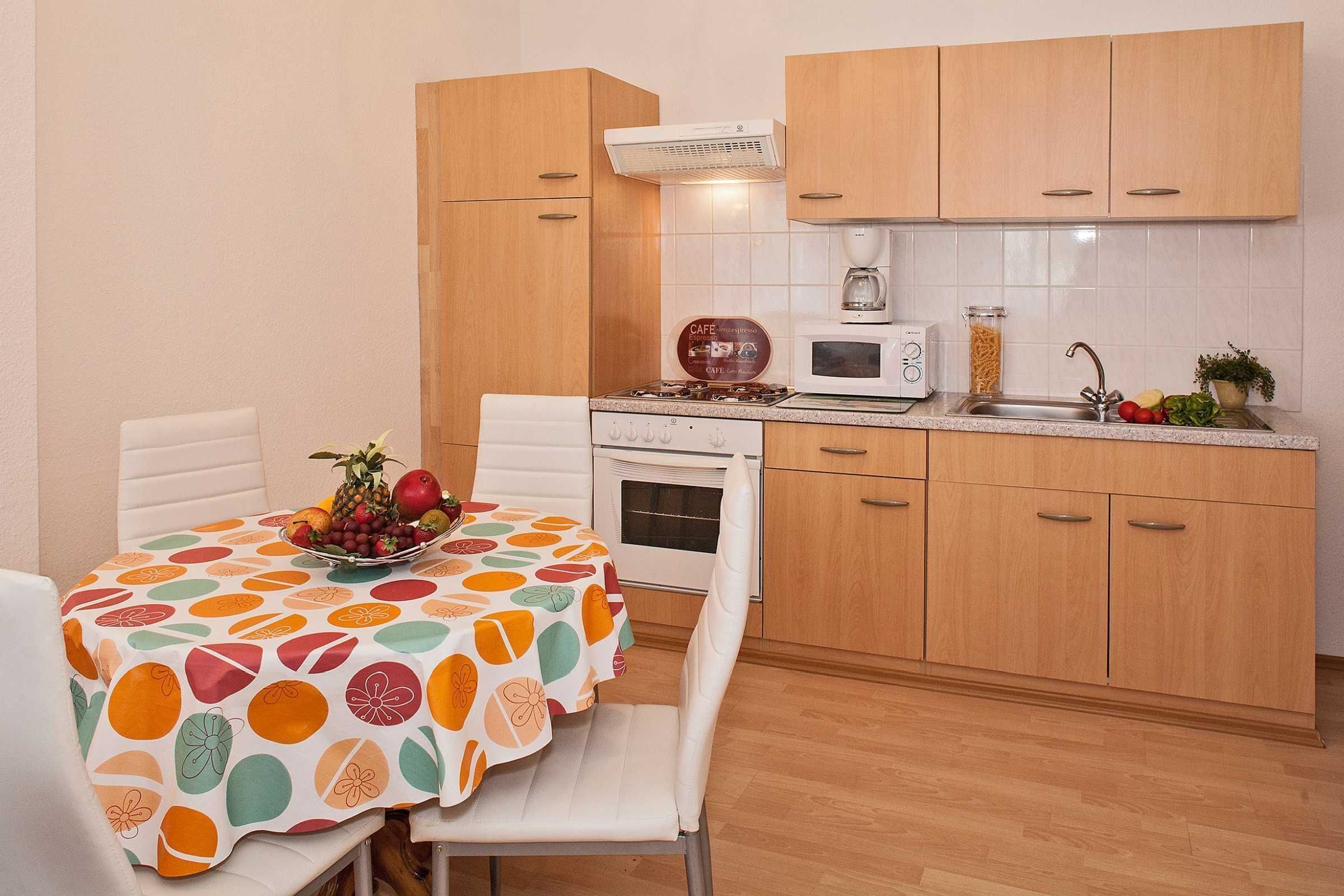 Una cocina compacta con armarios de madera, un microondas, una cafetera y una mesa de comedor con frutero.