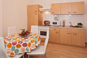 A compact kitchen with wooden cabinets, a microwave, a coffee maker, and a dining table with a fruit bowl.