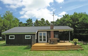 Een klein, gelijkvloers houten huisje met een terras en schoorsteen.