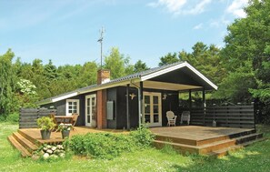 Een klein huis met een houten terras, een overdekte veranda en een schoorsteen.