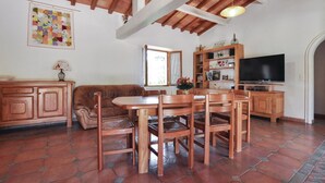 Una sala de estar acogedora con un sofá de cuero marrón, una mesa de comedor de madera y sillas, un televisor y una estantería.