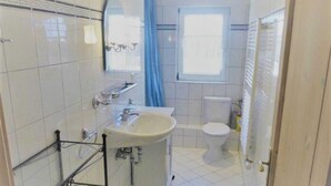 A bathroom with a sink, mirror, toilet, and a window with a curtain. - (129/9) 2-room apartment roof terrace + balcony - apartment house Plückhahn (Kühlungsborn)