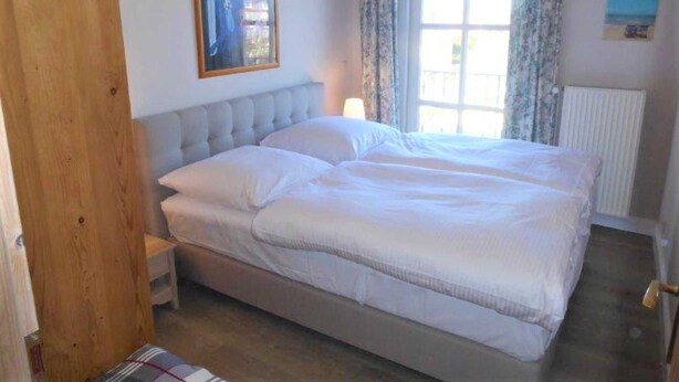 A bedroom with a large bed, a wooden door, a window with curtains, and a radiator. - (129/9) 2-room apartment roof terrace + balcony - apartment house Plückhahn (Kühlungsborn)