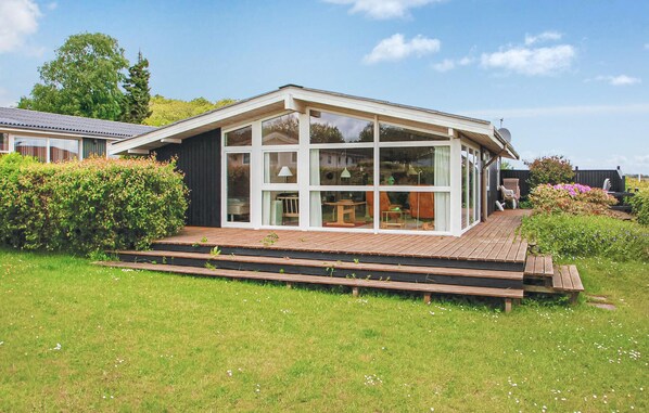 A modern house with a large glass front, a wooden deck, and a garden. - Lovely home in Bjert with house sea view (Bjert)
