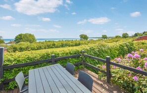 A wooden deck with a table and chairs, surrounded by a wooden fence and lush greenery. - Lovely home in Bjert with house sea view (Bjert)