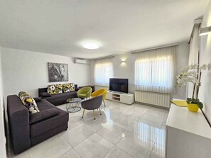Ein modernes Wohnzimmer mit einer Couch, Sesseln, einem Fernseher und einer Topfpflanze.
