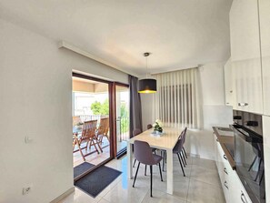 Eine moderne Küche mit Essbereich, ein Balkon mit Gartenmöbeln und ein großes Fenster mit Vorhängen.