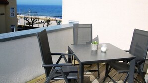 Un balcon avec une table et des chaises, donnant sur une plage et un immeuble.