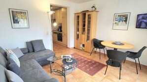 Un salon avec un canapé gris, une table basse et un coin repas comprenant une table ronde et des chaises.