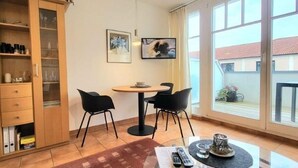 Un coin repas comprenant une table ronde, deux chaises, un buffet aux portes vitrées et une grande fenêtre donnant sur un paysage agréable.