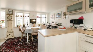 A well-lit kitchen with a dining area, featuring a wooden table, chairs, a clock, and various kitchen appliances. - Cozy home in Rønne with WiFi (Rønne)
