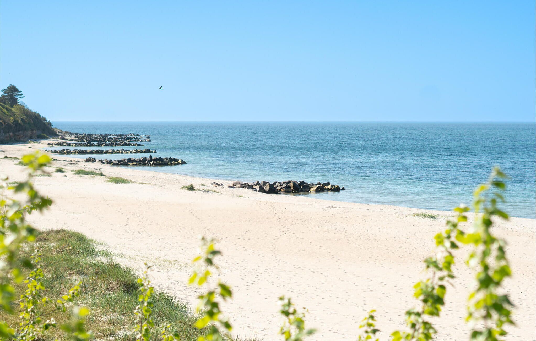 A beach with a clear sky, calm sea, and rocky outcrops.