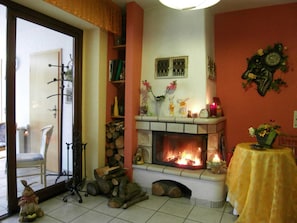 Un salon avec une cheminée, un fauteuil, une table sur laquelle est posé un vase et une horloge au mur.