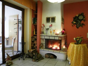 A living room with a fireplace, a chair, a table with a vase, and a clock on the wall.